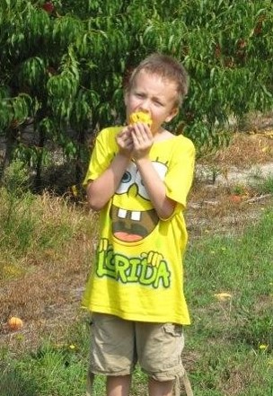 boy eating a peach in a peach orchard